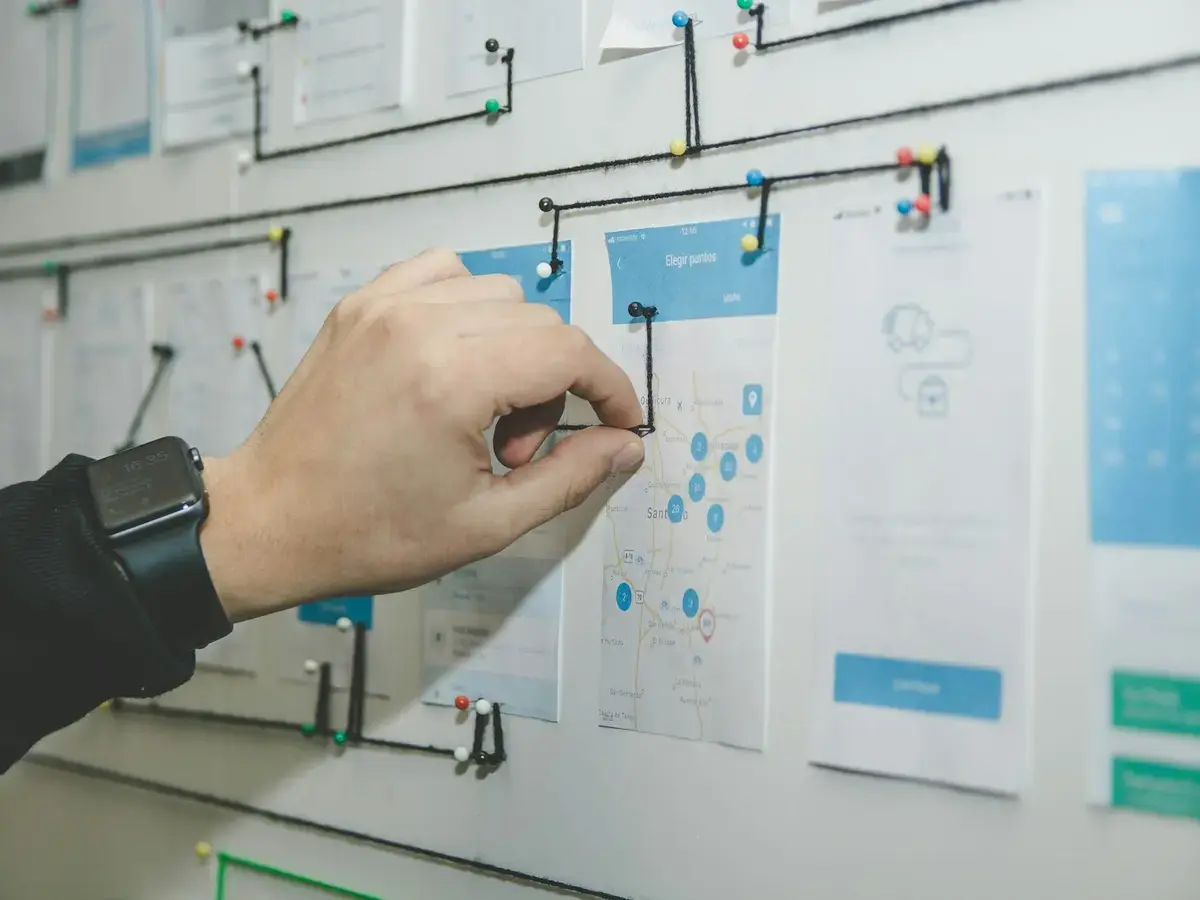Hand connecting printed app screens with thread, mapping a multi-role user flow
